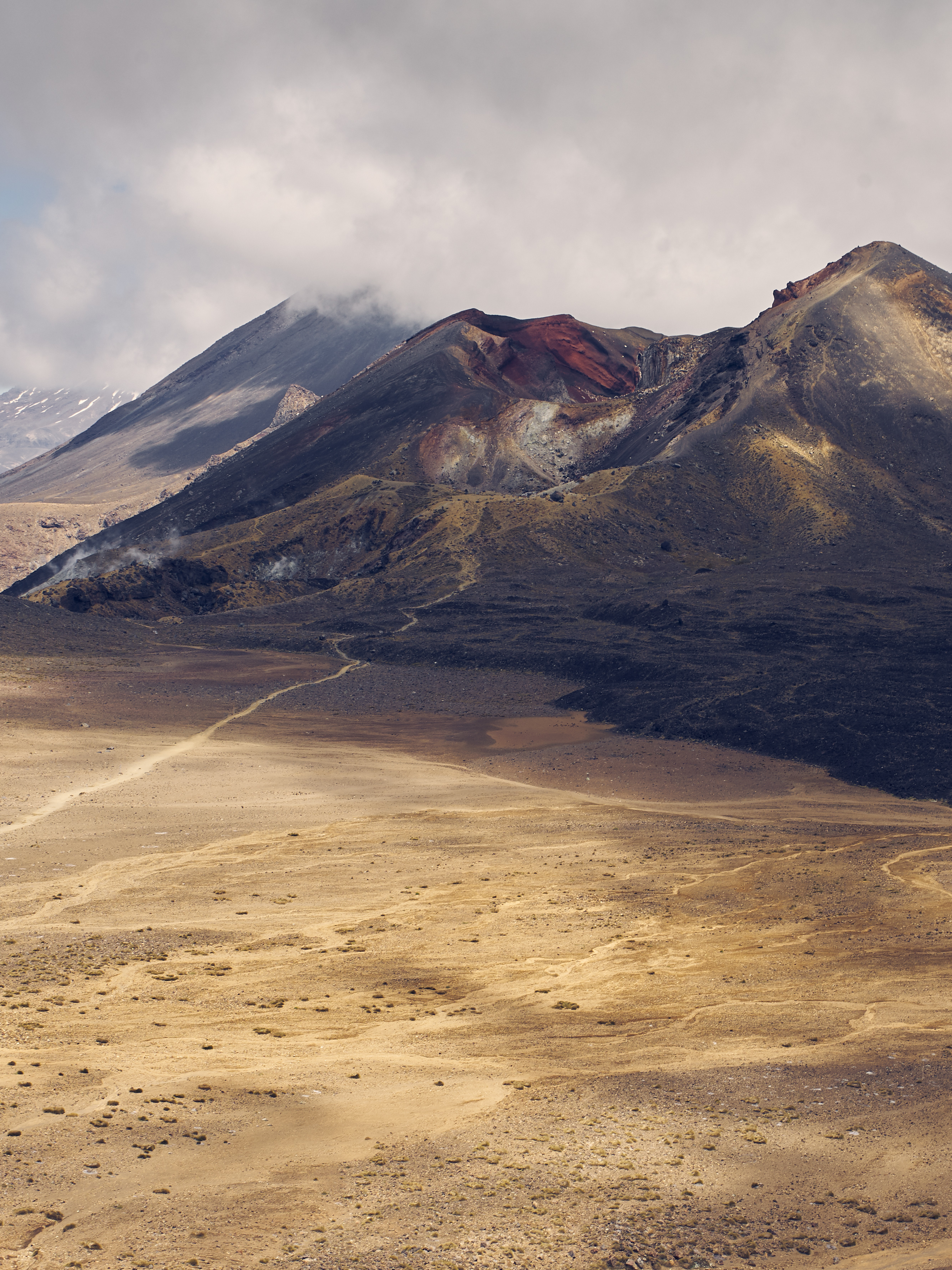 View from a panoramic viewpoint of ochre-colored plains and the red crater in the volcanic landscape of the Tongariro Crossing in the background