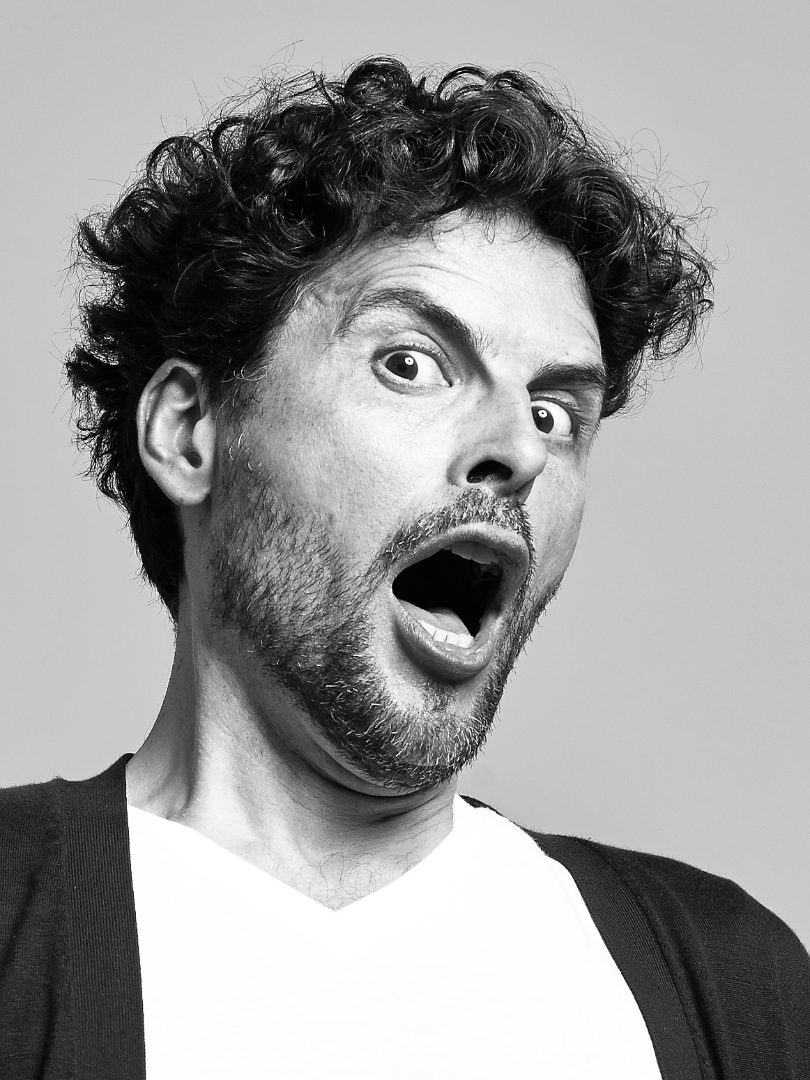 An Italian man with a very surprised look on his face with open mouth and eyes wide open,  displaying a mixture of surprise and astonishment.