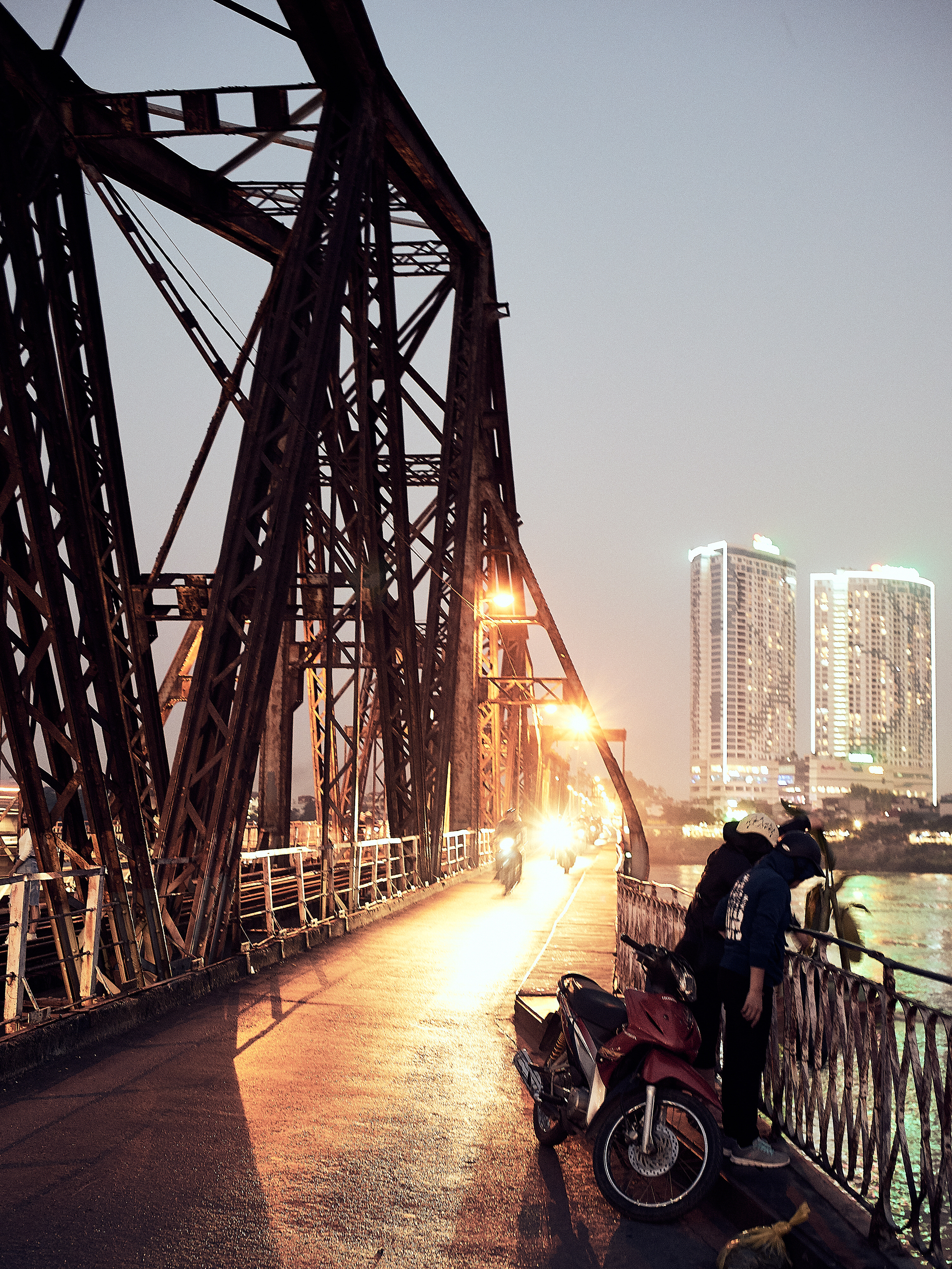 A couple with a motorcycle looking down Long Biên Bridge by night in Hanoi.