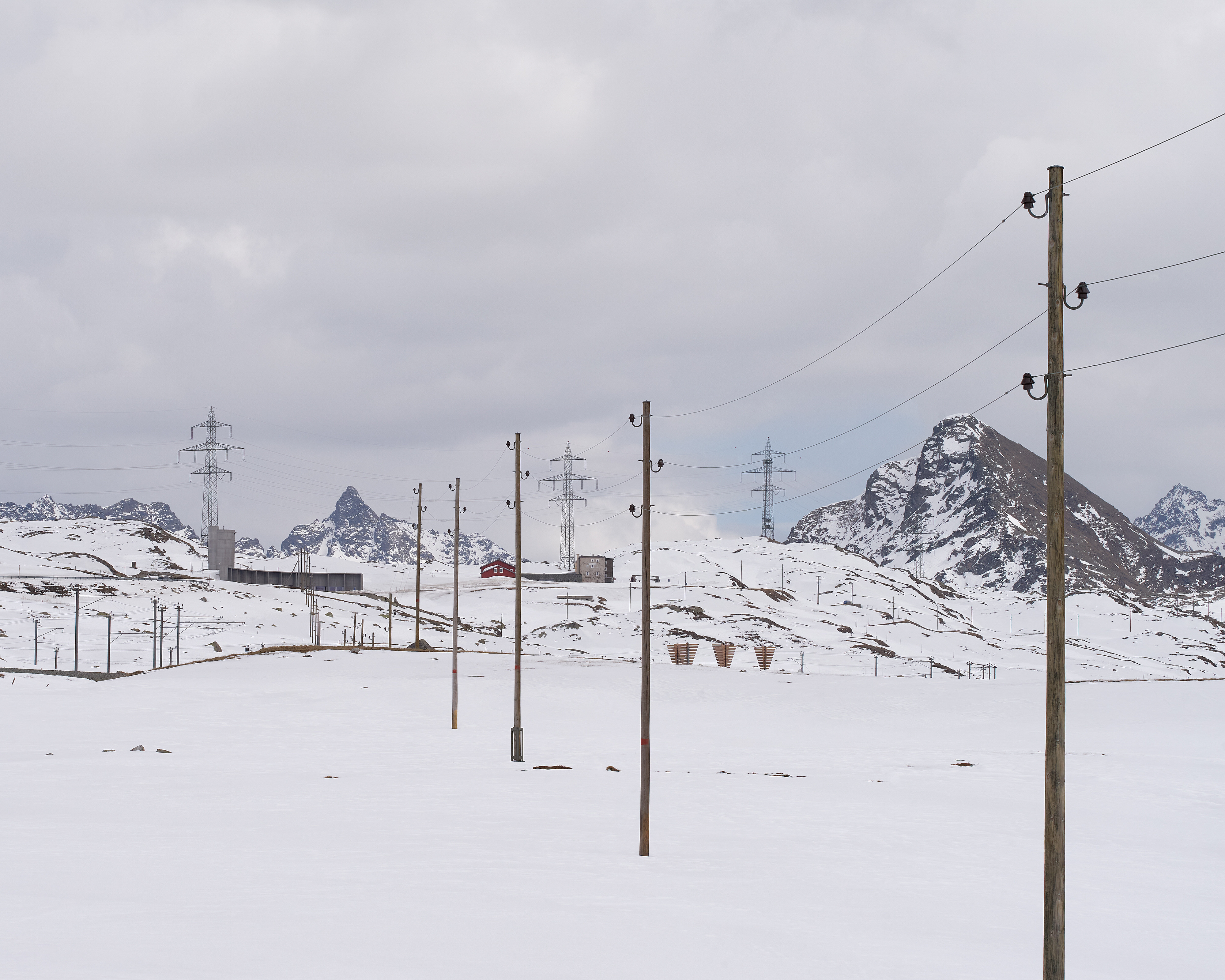 Scenic view of a snow-covered field featuring power lines and poles at a mountain pass against a backdrop of winter beauty.